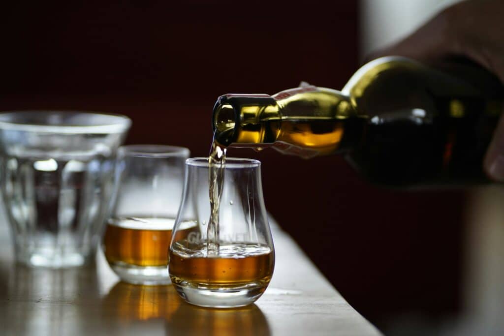 Whiskey being poured into two glass tumblers on a bar.
